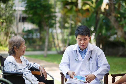 Asian doctor talking with elderly female patient on wheelchair