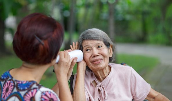 Daughter talking to hearing impaired elderly woman , using paper tube