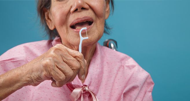 Caregiver take care asian elderly woman while using dental fross stick.