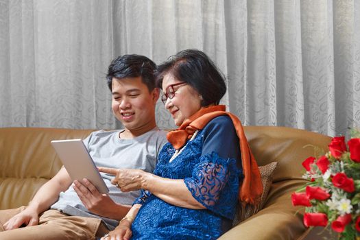 Adult son and senior mom sing a song while relaxed sitting on couch