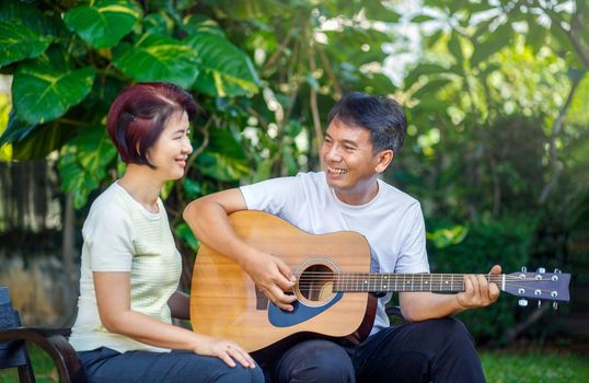 Middle aged  couple playing guitar while relax sitting on bench in backyard.