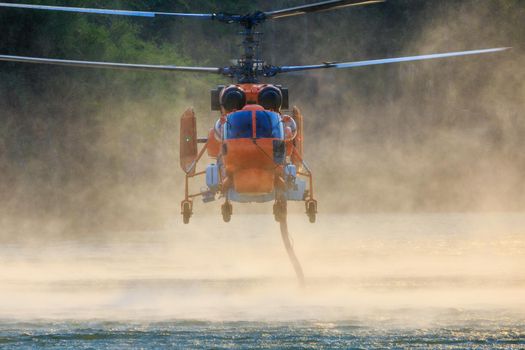 KA-32 Firefighting helicopter is hovering over the pond to refills water