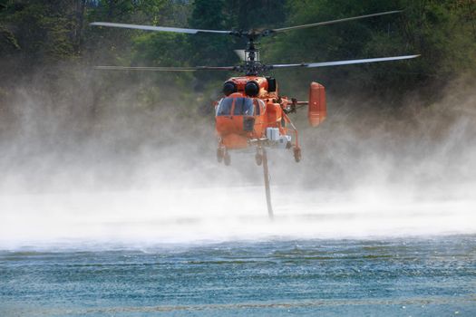 Firefighting helicopter is hovering over the pond to refills water