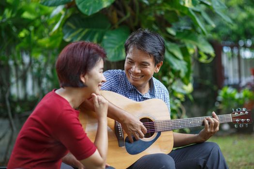 Middle aged  couple playing guitar while relax sitting on bench in backyard.