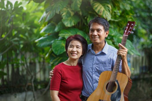 Middle aged  couple playing guitar while relax sitting on bench in backyard.