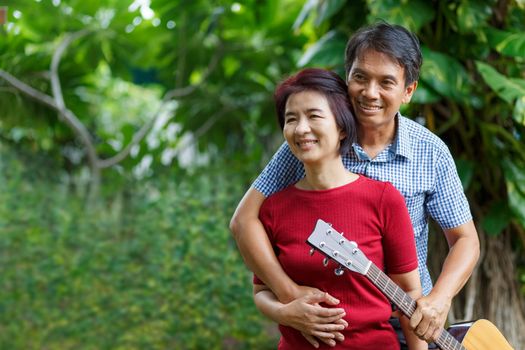 Middle aged  couple playing guitar while relax sitting on bench in backyard.