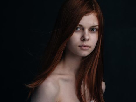 Portrait of a woman with red hair on a black background naked shoulders model. High quality photo