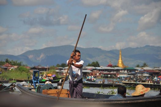 INLE LAKE, MYANMAR - 28 NOVEMBER 2016 View of ethnic man sailing boat pushing with long wooden pole from bottom on Inle lake in sunlight, Myanmar. Man sailing boat with pole