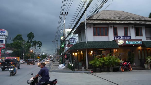 KOH SAMUI ISLAND, THAILAND - 21 JUNE 2019 Busy transport populated city street in cloudy day. Typical street full of motorcycles and cars. Thick blue clouds before storm during wet season