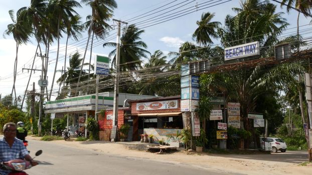 KOH SAMUI ISLAND, THAILAND - 24 JUNE 2019 Driving cars and small shops on roadside. Beach way and chain store Family mart on main road. Typical touristic village street. Thai people on motorbikes