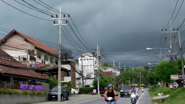 KOH SAMUI ISLAND, THAILAND - 11 JULY 2019 Busy transport populated city street in cloudy day. Typical street full of motorcycles and cars. Thick blue clouds before storm during wet season