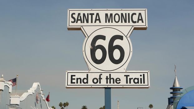 SANTA MONICA, LOS ANGELES, USA - 28 OCT 2019: Historic route 66, famous vintage california trip symbol. Pier of pacific ocean resort. Iconic retro road sign against the blue sky in amusement park.