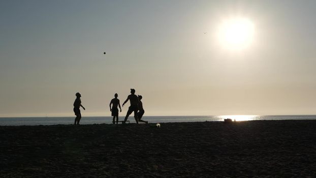 NEWPORT, LOS ANGELES CA USA - 3 NOV 2019: California summertime beach, young men playing roundnet or spike ball game with trampoline and having fun near pacific ocean. Silhouette against sunshine.