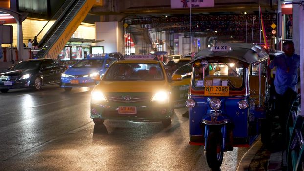 BANGKOK, THAILAND - 18 DECEMBER, 2018: Traditional Thai taxi - Tuk Tuk awaits tourists along the road. Night traffic of overpopulated city. Symbol of asian country, unique vehicle.