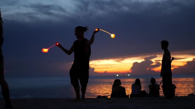 PHANGAN, THAILAND - 23 MARCH 2019 Zen Beach. Silhouettes of performers on beach during sunset. Silhouettes of young anonymous entertainers rehearsing on sandy beach against calm sea and sundown sky