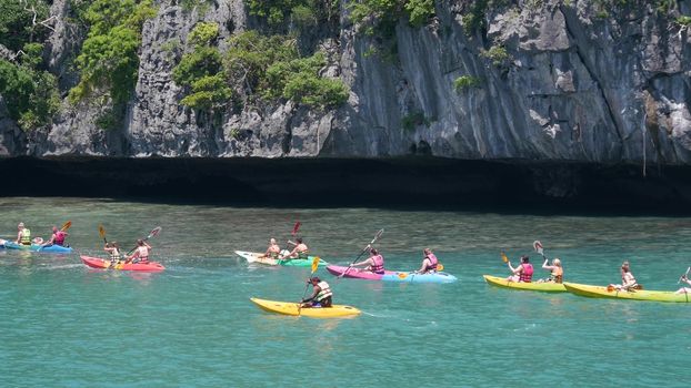 ANG THONG MARINE PARK, SAMUI, THAILAND - 9 JUNE 2019: People kayaking near cliff in paradise sea. Group of tourists paddling while riding kayaks on blue Idyllic turquoise ocean water near rocks