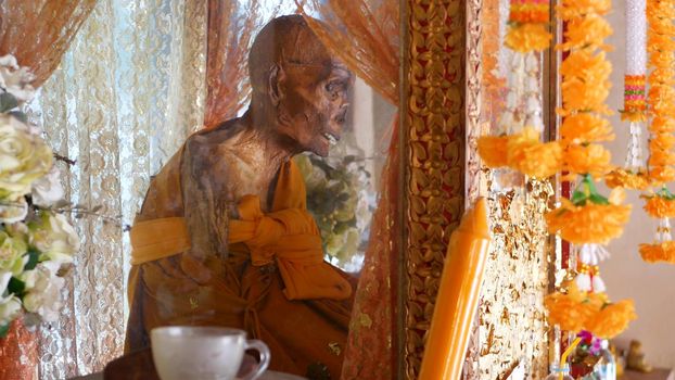 KOH SAMUI ISLAND, THAILAND - 17 JULY 2019: Wat Khiri Wongkaram Buddhist Temple. The mummified body of monk and gold leaf. Exotic tradition of storing the relics of saints who died during meditation