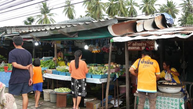 KOH SAMUI ISLAND, THAILAND - 10 JULY 2019: Food market for locals. Lively ranks with groceries. Typical daily life on the street in Asia. People go shopping for fruits vegetables, seafood and meat