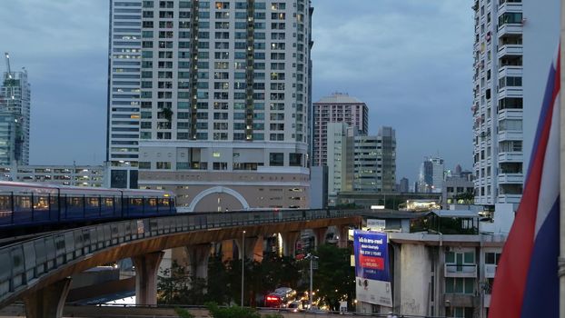 BANGKOK, THAILAND - 10 JULY, 2019: View of modern asian city from bts sky train platform. Train on metro rail road station. Public transportation in Krungtep downtown. State national flag waving