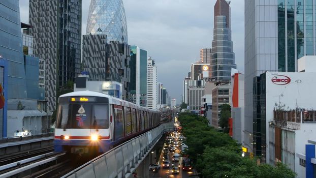 BANGKOK, THAILAND - 10 JULY, 2019: View of modern asian city from bts sky train platform. Train on metro rail road station. Public transportation in Krungtep downtown. Evening steet traffic in Asia