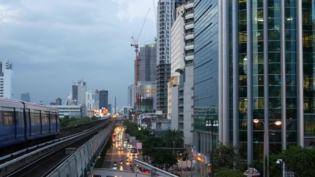 BANGKOK, THAILAND - 10 JULY, 2019: View of modern asian city from bts sky train platform. Train on metro rail road station. Public transportation in Krungtep downtown. Evening steet traffic in Asia