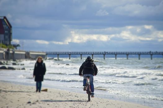 Zelenogradsk, Russia. An elderly woman walks along the sandy beach towards the cyclist.