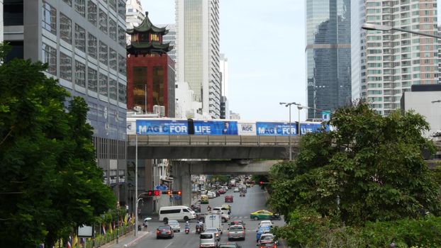 BANGKOK, THAILAND - 13 JULY, 2019: Traffic on modern city street. Contemporary train riding on railroad bridge over road with cars in center of capital
