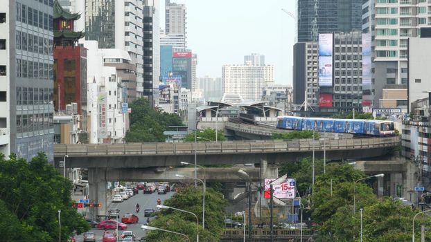 BANGKOK, THAILAND - 13 JULY, 2019: Traffic on modern city street. Contemporary train riding on railroad bridge over road with cars in center of capital