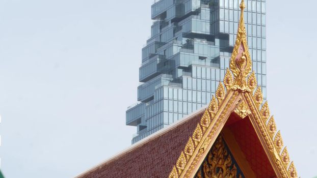 BANGKOK, THAILAND - 13 JULY, 2019: Conceptual contrast of oriental old traditional ancient temple and modern new futuristic Mahanakhon skyscraper. Classic buddhist wat compared to urban cityscape