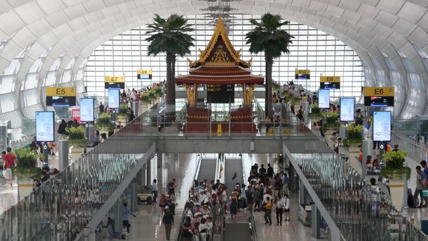 BANGKOK, THAILAND - 16 JULY, 2019: Oriental structure in airport. Traditional Thai construction mounted on glass platforms inside crowded terminal, Suvarnabhumi Airport people whaiting for boarding.