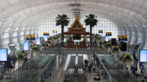 BANGKOK, THAILAND - 16 JULY, 2019: Oriental structure in airport. Traditional Thai construction mounted on glass platforms inside crowded terminal, Suvarnabhumi Airport people whaiting for boarding.