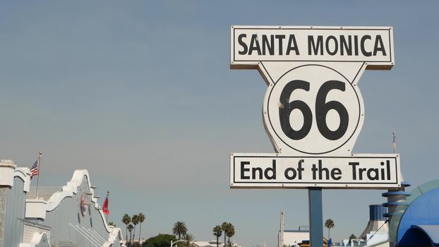 SANTA MONICA, LOS ANGELES, USA - 28 OCT 2019: Historic route 66, famous vintage california trip symbol. Pier of pacific ocean resort. Iconic retro road sign against the blue sky in amusement park.