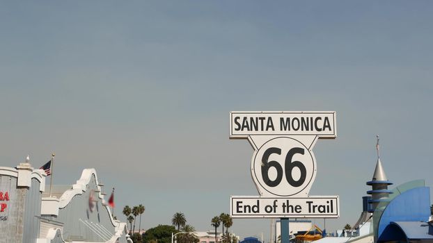SANTA MONICA, LOS ANGELES, USA - 28 OCT 2019: Historic route 66, famous vintage california trip symbol. Pier of pacific ocean resort. Iconic retro road sign against the blue sky in amusement park.