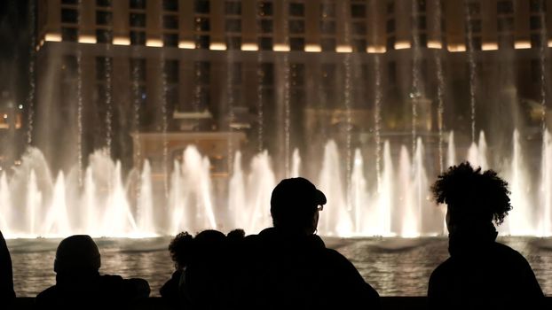 LAS VEGAS, NEVADA USA - 13 DEC 2019: People looking at Bellagio fountain musical performance at night. Contrast silhouettes and glowing dancing splashing water. Entertainment show in gambling city.