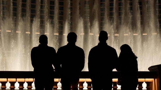 LAS VEGAS, NEVADA USA - 13 DEC 2019: People looking at Bellagio fountain musical performance at night. Contrast silhouettes and glowing dancing splashing water. Entertainment show in gambling city.