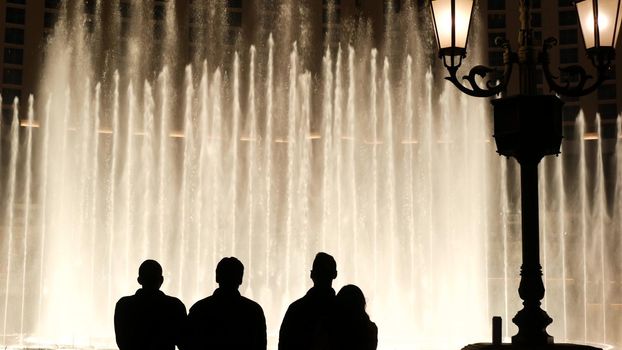 LAS VEGAS, NEVADA USA - 13 DEC 2019: People looking at Bellagio fountain musical performance at night. Contrast silhouettes and glowing dancing splashing water. Entertainment show in gambling city.