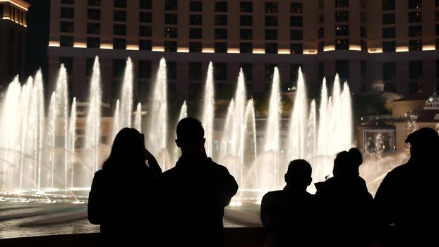 LAS VEGAS, NEVADA USA - 13 DEC 2019: People looking at Bellagio fountain musical performance at night. Contrast silhouettes and glowing dancing splashing water. Entertainment show in gambling city.