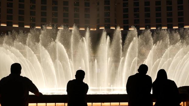 LAS VEGAS, NEVADA USA - 13 DEC 2019: People looking at Bellagio fountain musical performance at night. Contrast silhouettes and glowing dancing splashing water. Entertainment show in gambling city.