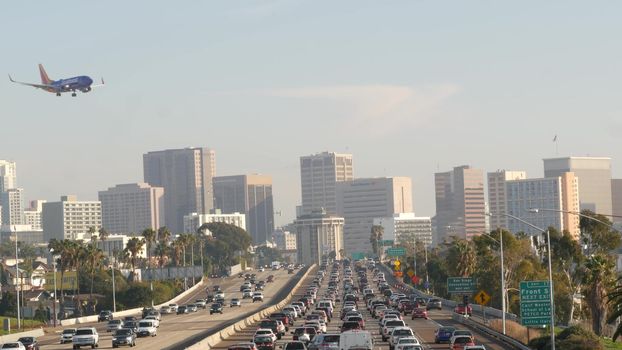 SAN DIEGO, CALIFORNIA USA - 15 JAN 2020: Busy intercity freeway, traffic jam on highway during rush hour. Urban skyline, highrise skyscraper and landing plane. Flying airplane, transportation concept.