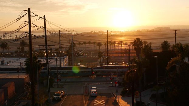 SAN DIEGO, CALIFORNIA USA - 15 JAN 2020: Level crossing near Lindbergh field international airport. Coaster railroad train and runway at sunset. NCTD rail transportation, cars and railway transport.