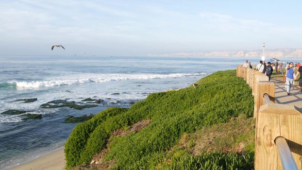 La Jolla, San Diego, CA USA -24 JAN 2020: Group of people walking on steep high cliff promenade, multiethnic pedestrians, tourists during holidays. Succulents and ocean, golden sunset in California.