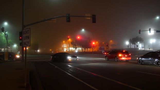 VISTA, CALIFORNIA USA - 24 JAN 2020: Marine layer, dense fog on driveway crossroad at night. June gloom, misty nebulous bad weather. Dangerous low visibility on road intersection. Car traffic safety.