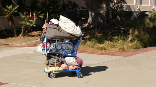 SAN DIEGO, CALIFORNIA USA - 30 JAN 2020: Stuff of homeless street people on walkway, truck on roadside. Begging problem in downtown of city near Los Angeles. Jobless beggars trolley cart on pavement.