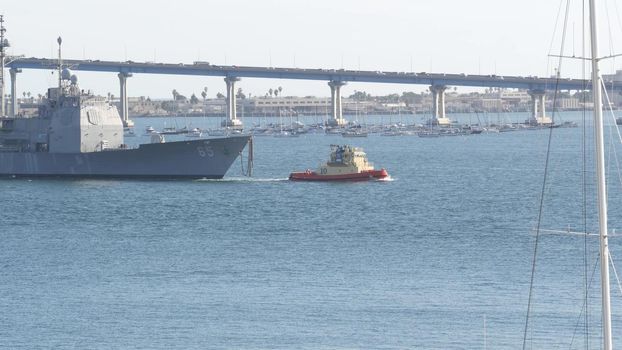 SAN DIEGO, CALIFORNIA USA - 13 FEB 2020: Tugboat pulling USS Chosin CG-65, military warship of US Navy fleet. Tug towing maritime battleship in port harbor. United States Armed Forces naval ship.