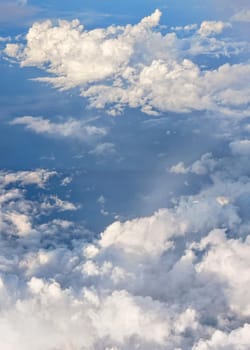 Fluffy sky clouds lit by afternoon sun, as seen from commercial airplane flying over.