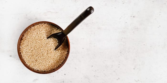 White sesame - Sesamum indicum - seeds in small wooden cup on white stone like board, view from above, space for text right side.