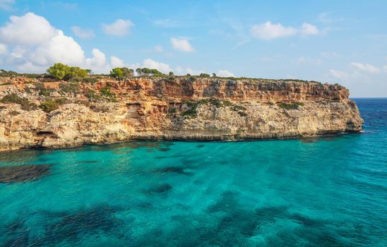 Clear blue green sea water, rocky cliffs around - nice sunny day at Ansa de s'Estri, Mallorca.