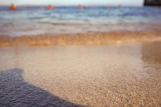 Golden beach sand washed by sea water lit by morning sun, low angle closeup detail - abstract shallow depth of field marine background, only few grains in focus.