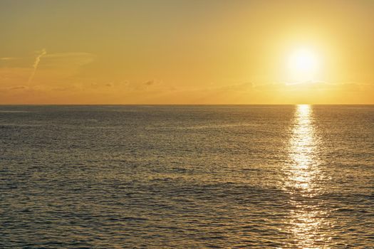 Sun rising above calm sea, clouds coloured to orange.