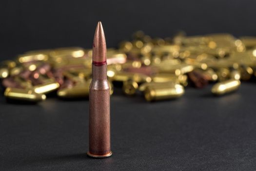 Copper machine gun bullet, more blurred yellow ammo on black board background.